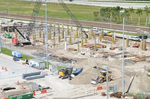 Aerial view of an airport terminal construction site with cranes, piling equipment, and formwork