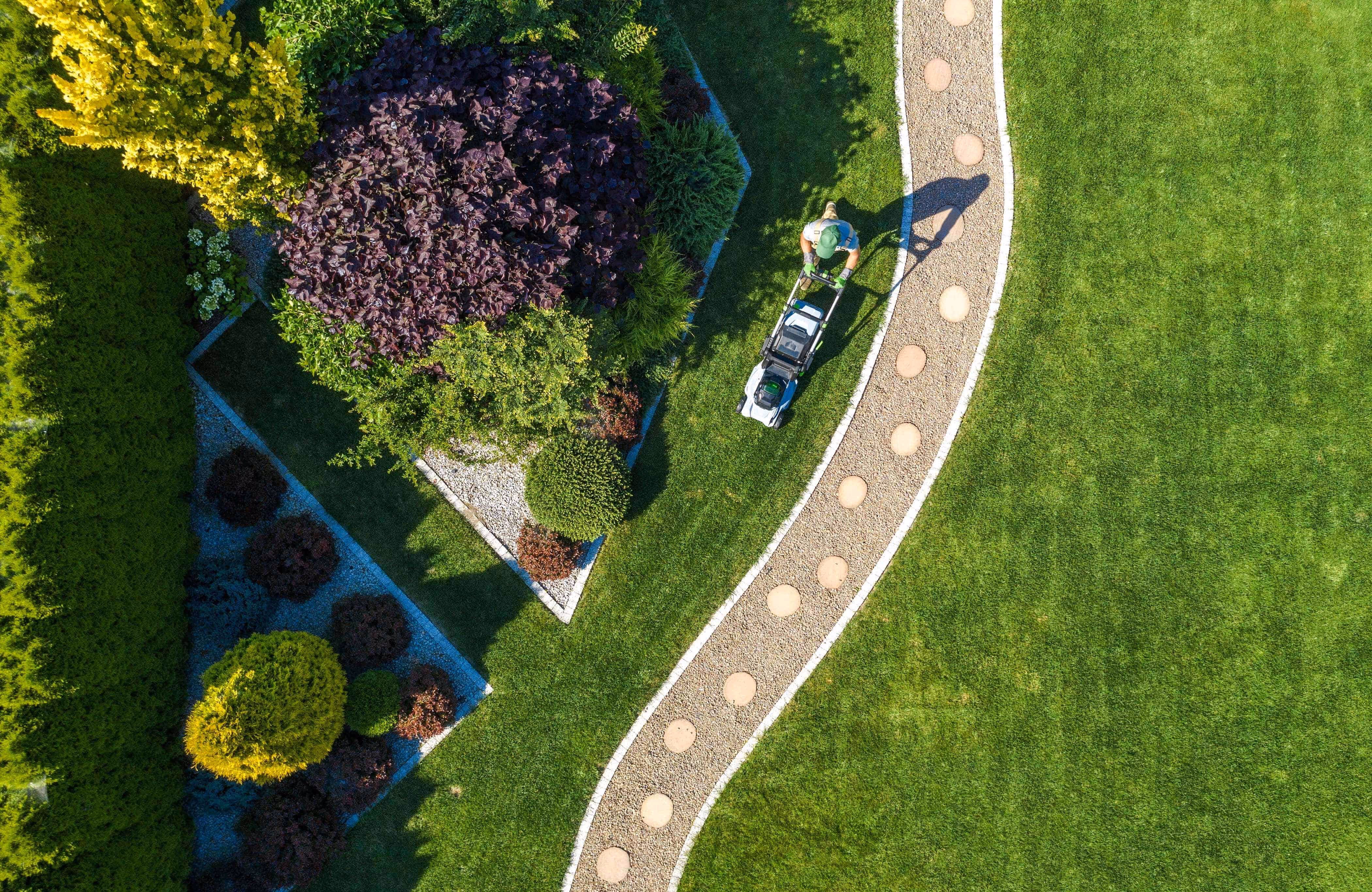 Landscaper mowing a lawn beside a curved paver path and planted garden beds