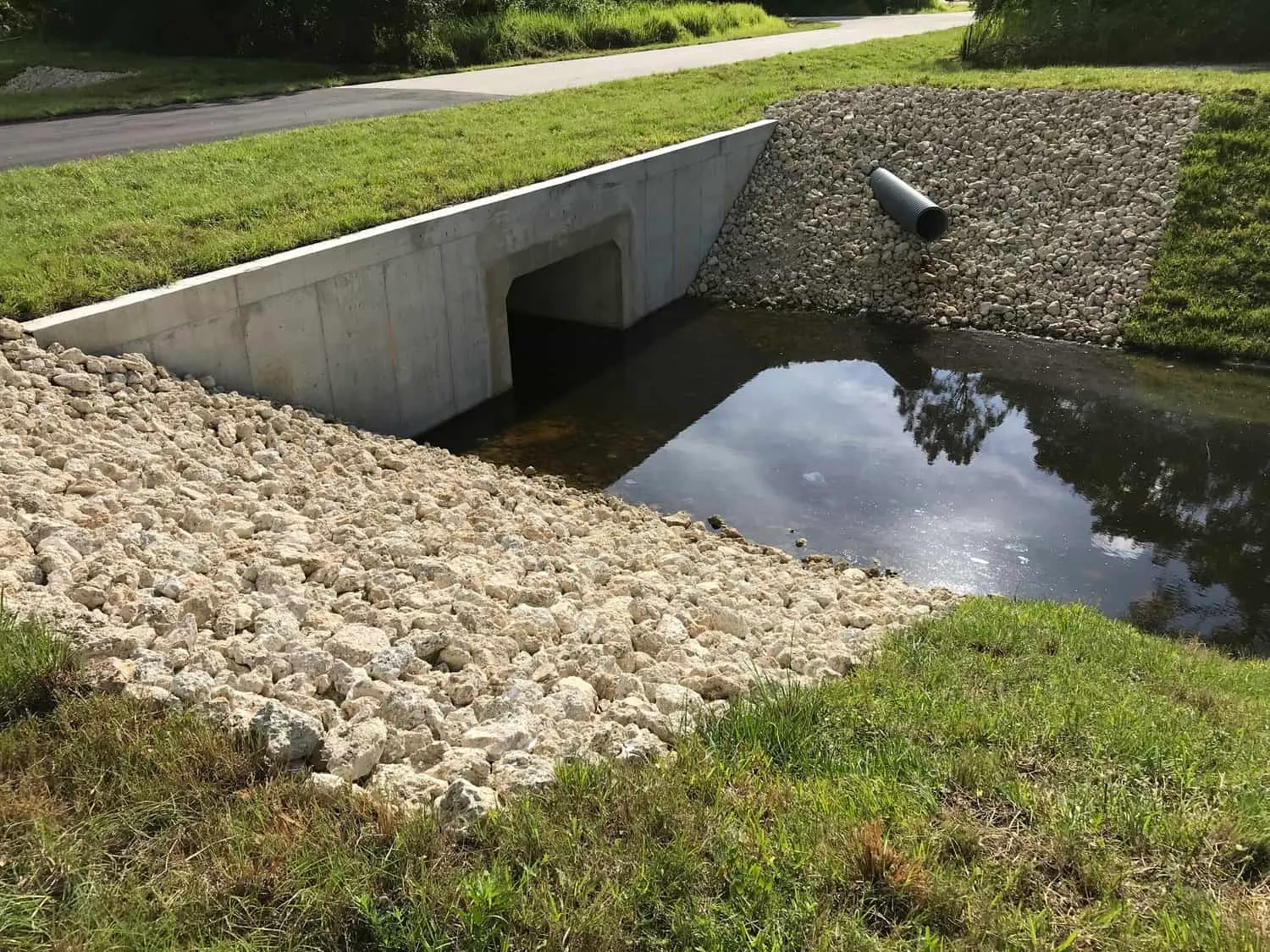 Finished concrete box culvert headwall at a canal crossing, with rock rip-rap and a drainage pipe