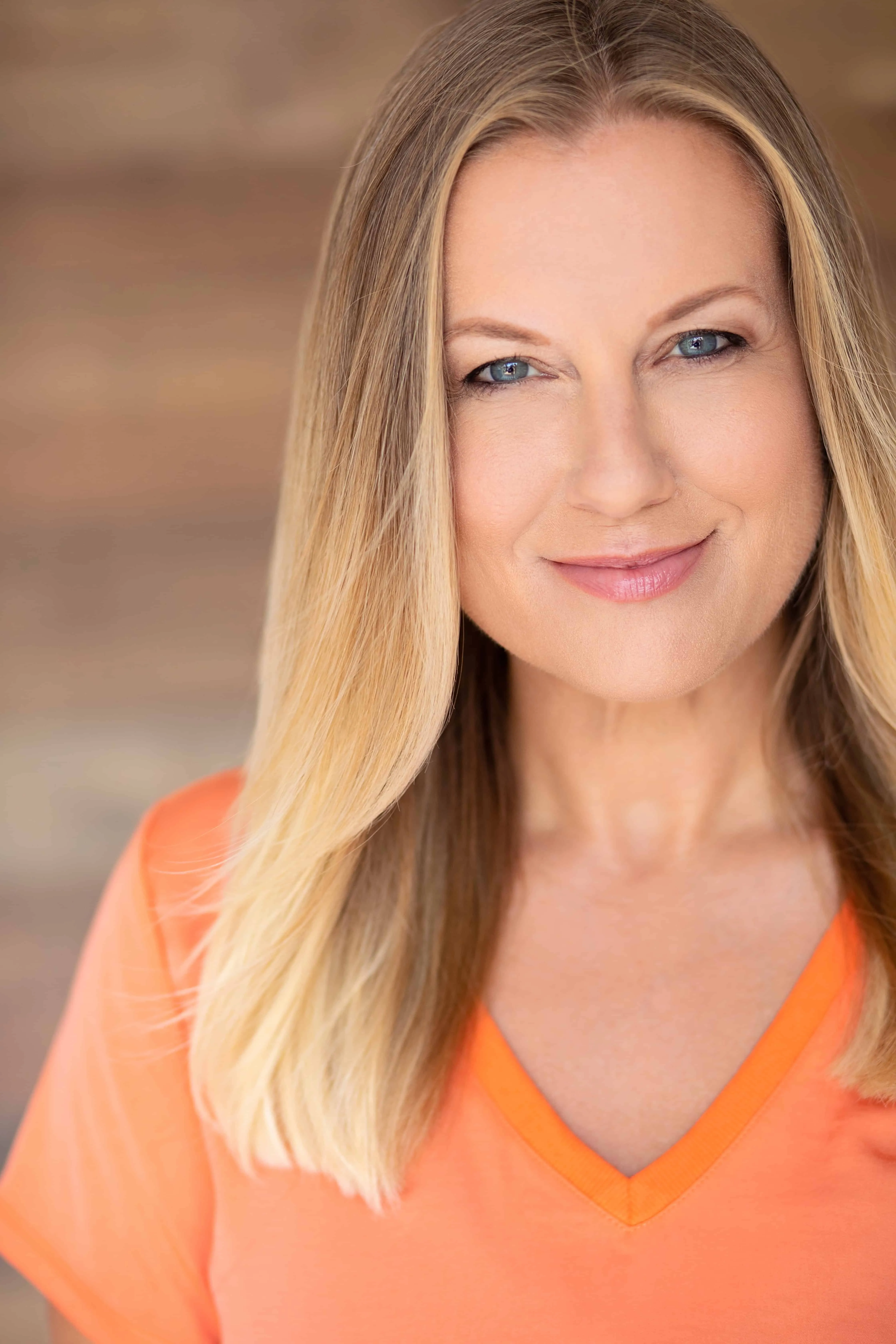 Studio headshot of Tami Riely smiling in an orange top