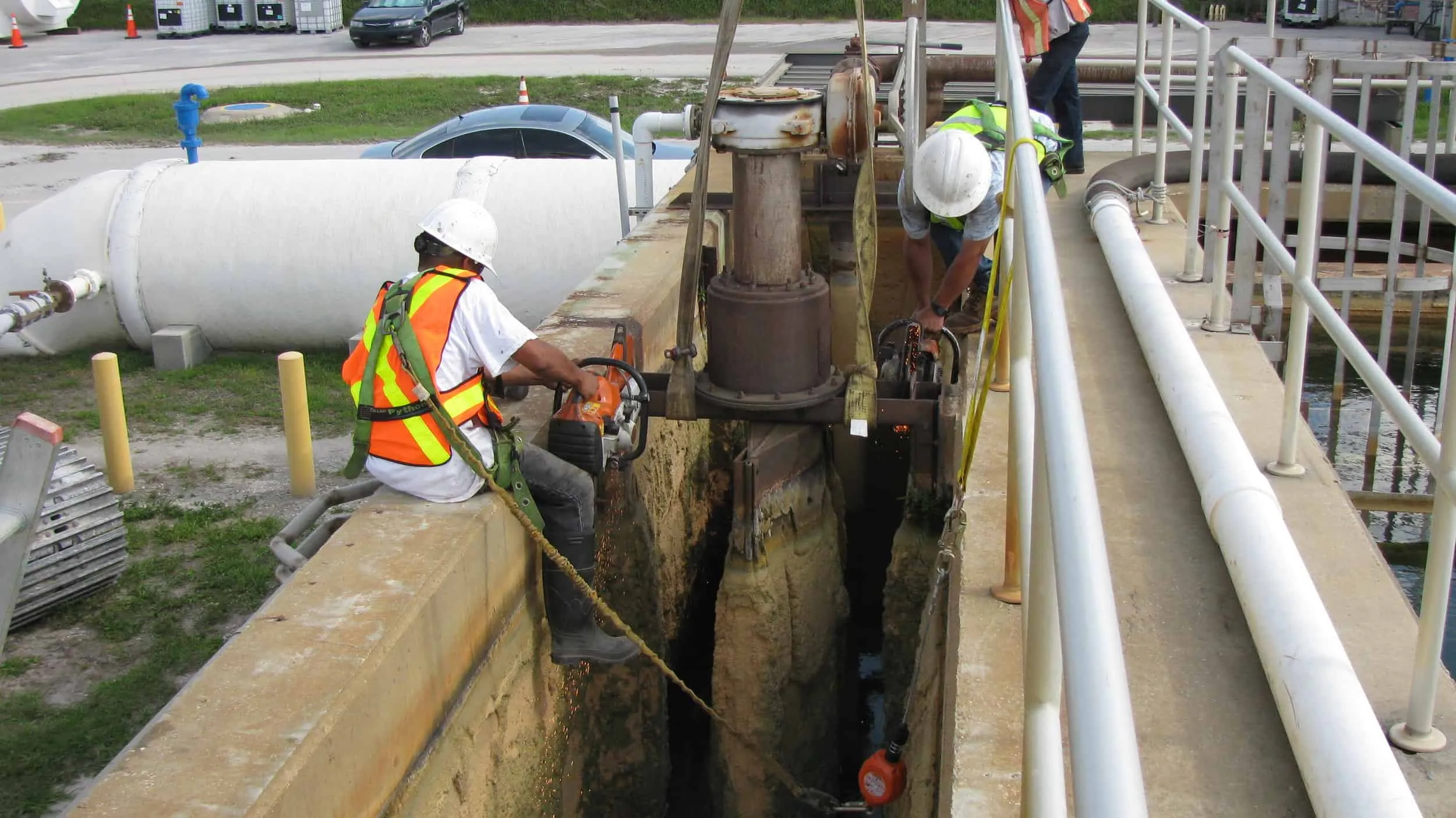 Workers using a cutting tool on treatment plant infrastructure at an elevated concrete platform