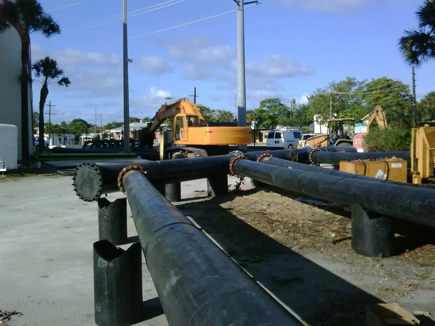 Rows of large black pipes at a treatment plant site with an excavator in the background
