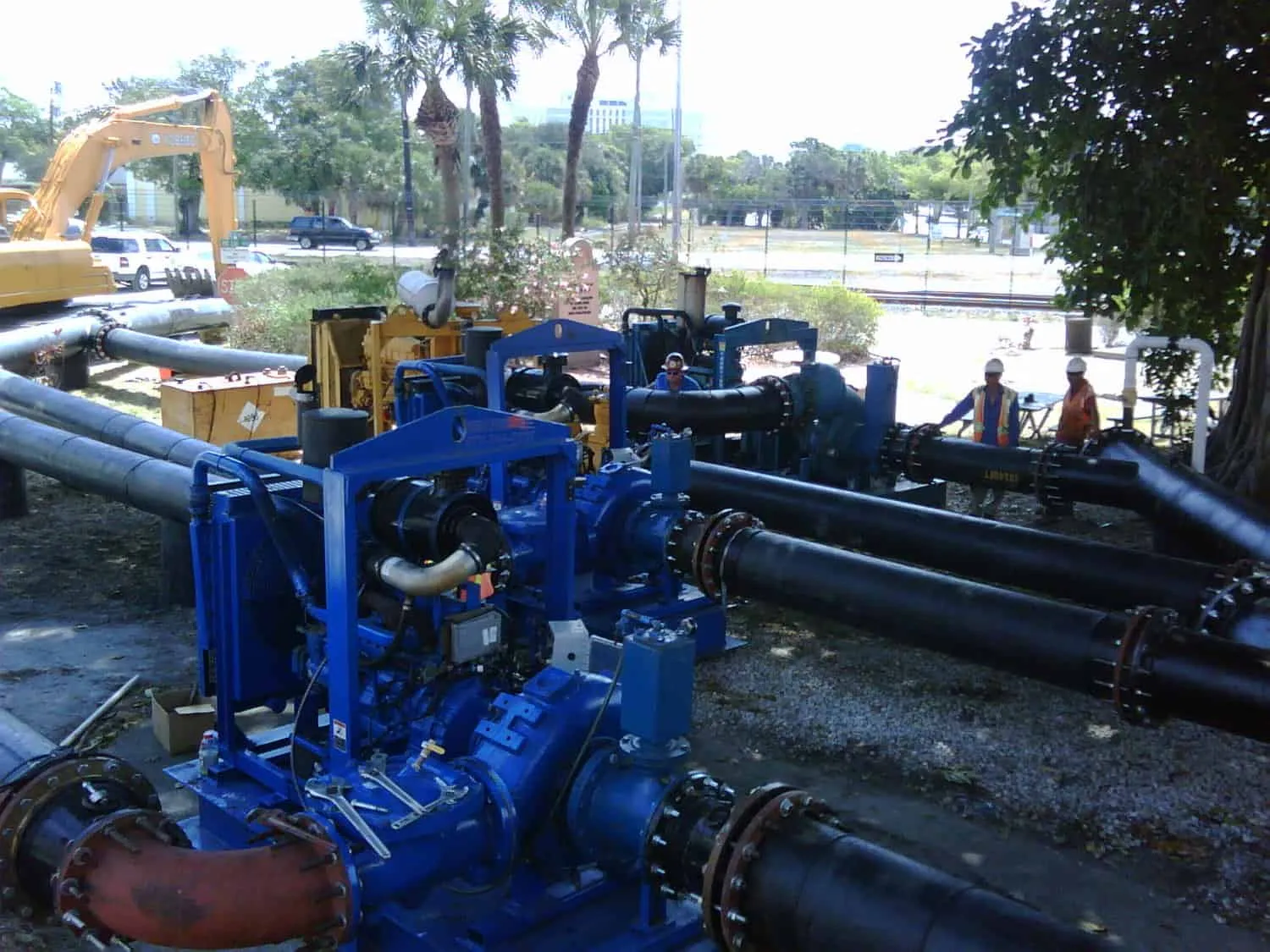 Blue pump and generator equipment connected to black and red pipes at an outdoor treatment plant site